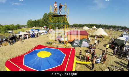 RUSSIA, NELIDOVO - JUL 12, 2014: Young boy jumps from tower to inflated deck during fair at sunny summer day. Aerial view. Photo with noise from actio Stock Photo