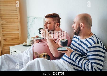 A gay couple and their French Bulldog lounging on a bed. Stock Photo
