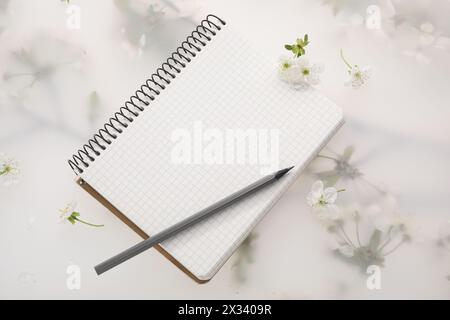 Guest list. Notebook, pencil and beautiful cherry tree blossoms on spring floral background, flat lay Stock Photo