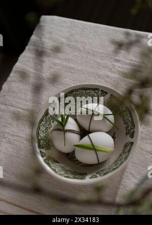 Easter. Three white decorated eggs in a green bowl on a beige background, shot from above. Stock Photo