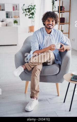Photo of cheerful positive guy dressed plaid shirt drinking hot beverage enjoying weekend indoors room home house Stock Photo