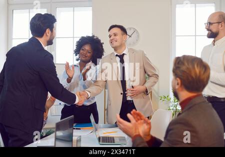 Team of business professionals applauding after successful handshake between two colleagues. Stock Photo