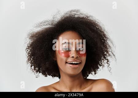 A beautiful young African American woman with curly hair showcasing eye patches in a studio, embodying a skin care concept. Stock Photo