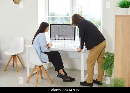 Young interior designers man and woman looking floor plan of new house on computer monitor screen. Stock Photo