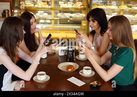 Four pretty women sit in cafe with phones, focus on right and left girls Stock Photo