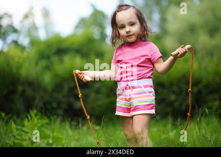 Little cute girl poses with skipping rope in summer sunny garden Stock Photo