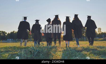 Graduate students walking through an evening meadow at sunset. Stock Photo