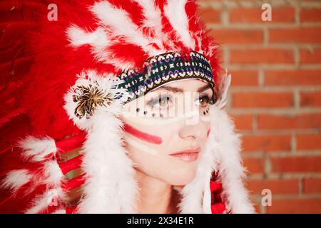 Closeup portrait of young woman dressed in hat made of red and white feathers. Stock Photo