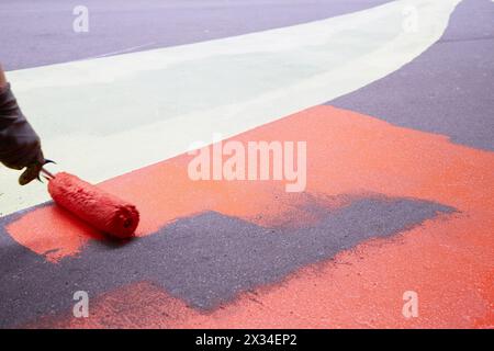 Worker paints asphalt with paint roller in different colours. Stock Photo