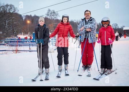 Family portrait of four skiers standing at ski resort in evening. Stock Photo