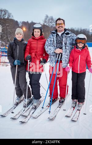 Family portrait of four skiers standing at ski resort in evening. Stock Photo