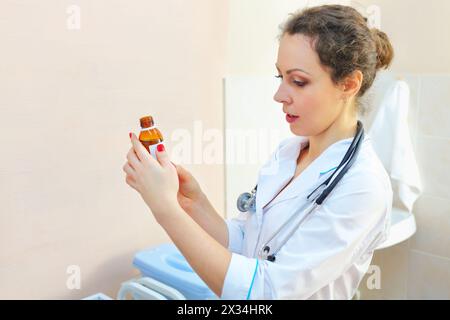 nurse in white coat holds vial with drug and reads inscription on label Stock Photo