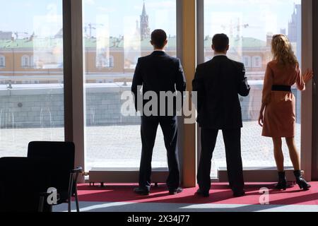Group of businessmen: two men and a woman standing near big window with view of the Kremlin Stock Photo