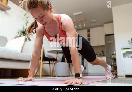 Strong woman doing plank exercises at home. Workout at home. Real domestic life of female athlete. Stock Photo