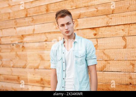 Young Handsome Man In A Denim Dress Near The Wooden Wall Stock Photo