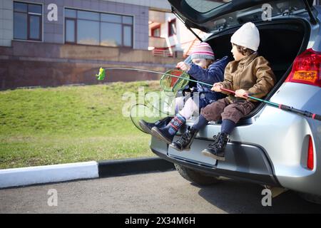 Two children are sitting in open trunk with fishing rod and net Stock Photo