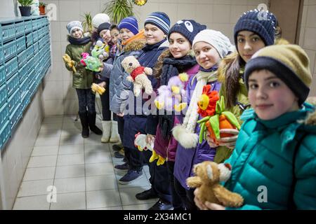Group of ten children stands holding fluffy toys at mailboxes in entrance hall of residential house. Stock Photo