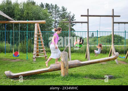 Mother with son and daughter swinging on a swing on a wooden playground Stock Photo