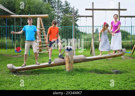 Parents with son and daughter teetering on a swing on a wooden playground Stock Photo