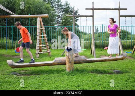 Mother with son and daughter teetering on a swing on a wooden playground Stock Photo