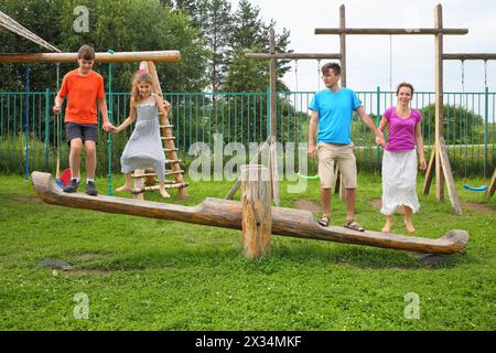Parents with son and daughter happy jumping on a swing on a wooden playground Stock Photo