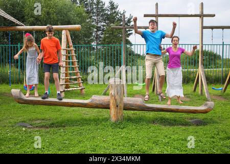 Parents with son and daughter jumping on a swing on a wooden playground Stock Photo