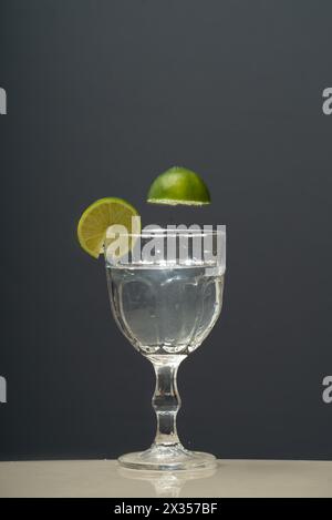a glass cup with clear water and two slices of lemons falling inside. Stock Photo