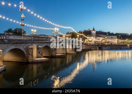 Old bridge over the Nabão River and the city of Tomar in Portugal lit up in celebration at dusk. Stock Photo