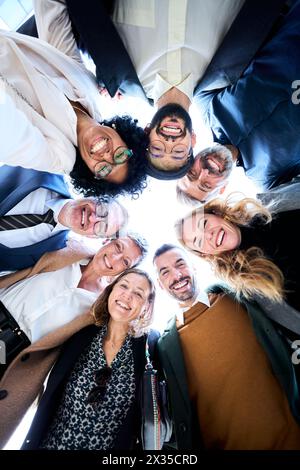 A group of diverse business people in formal wear gathered in a circle smiling and stacking hands Stock Photo