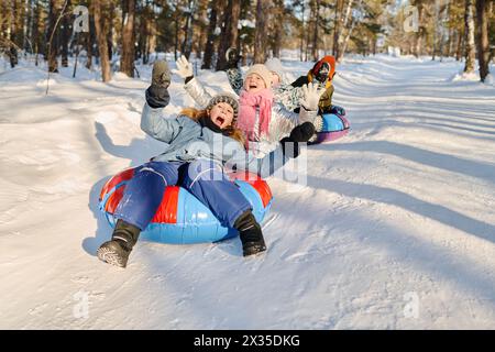 Group of joyful kids in winterwear screaming while moving down hill on snow tubes and slides and enjoying spending time together Stock Photo