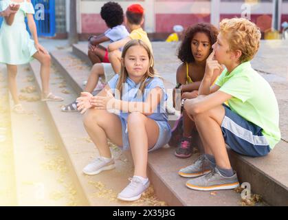 Positive tweenagers friendly blabbing while sitting on steps outdoors Stock Photo