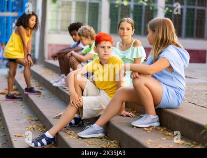 Happy tweenagers friends sitting on steps outdoors and chatting Stock Photo
