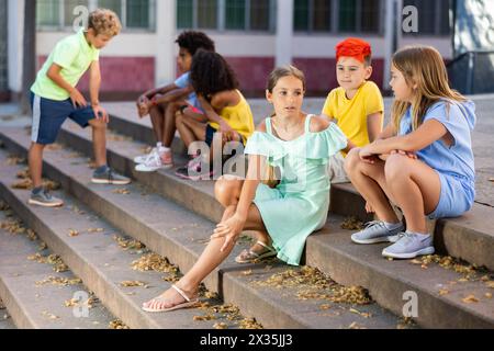 Positive tweenagers friendly blabbing while sitting on steps outdoors Stock Photo