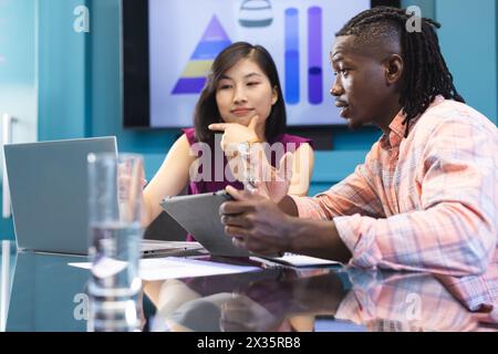 A diverse colleagues, African American man and an Asian woman, are discussing work in a modern busin Stock Photo