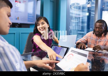 Diverse team discussing work in a modern business office, Asian woman showing tablet Stock Photo