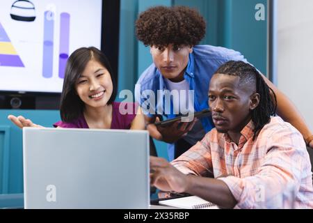 Diverse group of young colleagues focusing on laptop screen in a modern business office Stock Photo