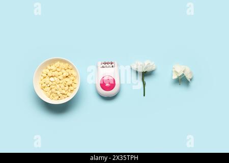 Modern epilator with wax and flowers on blue background Stock Photo