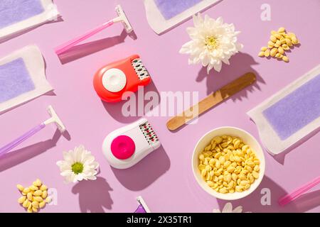 Modern epilators with razors, wax and flowers on lilac background Stock Photo