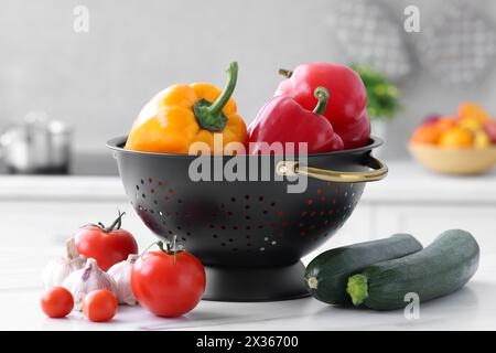 Black colander and different vegetables on white marble table in kitchen Stock Photo