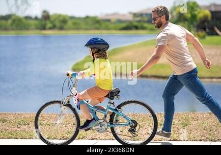 Father and son learning to ride a bicycle having fun together at Fathers day. Father teaching his son cycling on bike in american neighborhood. Father Stock Photo