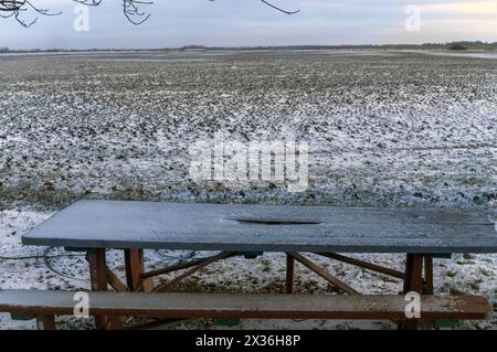 a handcrafted wooden bench and table and an endless arable land in the background, covered with snow Stock Photo