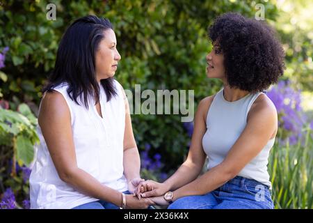 Mother and daughter sitting at home in garden, holding hands Stock Photo