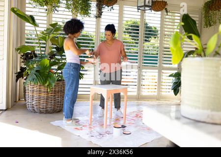 Mature biracial mother, adult daughter paint furniture in an upcycling project at home Stock Photo