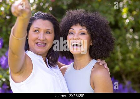 Mature biracial mother points, young daughter smiles beside her in garden Stock Photo