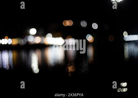 Colorful bokeh of lights reflecting on water surface at dark black night Stock Photo
