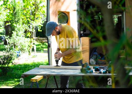 Caucasian man sanding a wooden strip to camperize a customized van Stock Photo