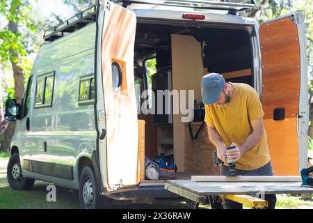 Man sanding wood with an electric sander customizing a camper van Stock Photo