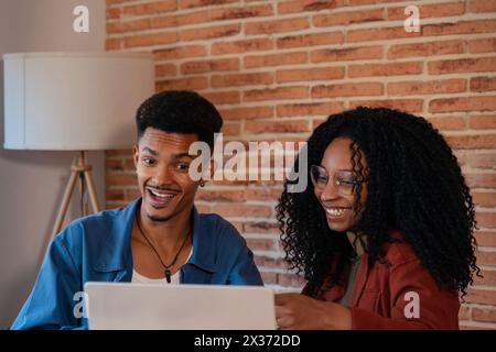 Happy multiethnic man and woman have fun browsing internet on laptop indoors. Stock Photo