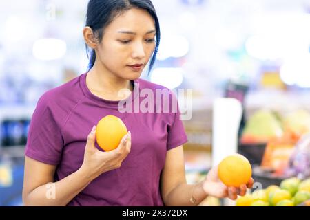 A young woman in a store chooses fresh oranges Stock Photo