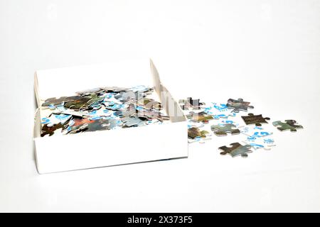 In the picture there is a box with puzzles and several pieces of puzzles lying next to the box. Stock Photo
